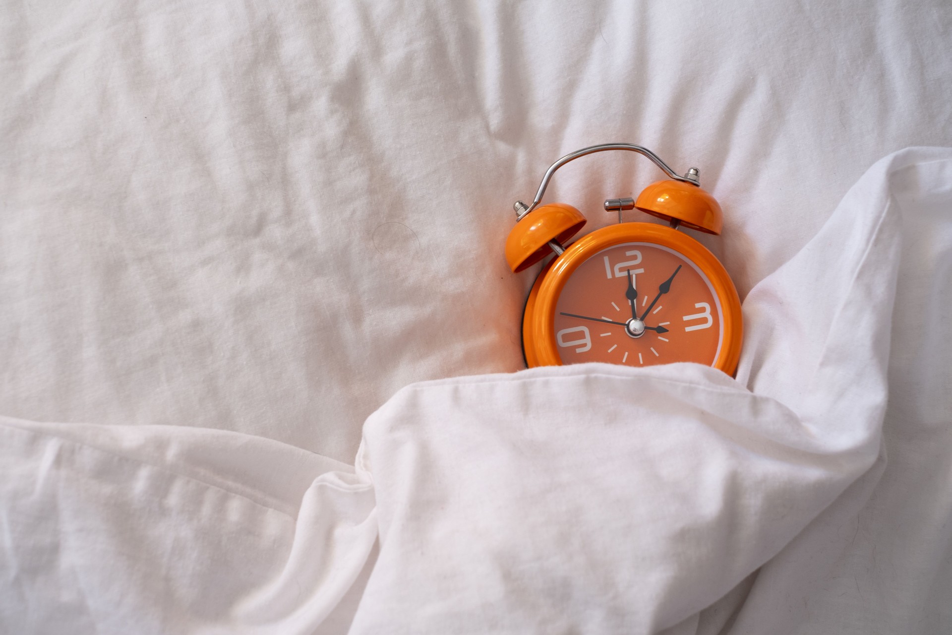 Orange alarm clock on white bed. Fashionable minimalist style. Time, business and technology concept. Flat lay composition. Top view